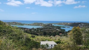 Un paysage côtier avec une maison au premier plan, une baie avec des bateaux et un ciel dégagé.