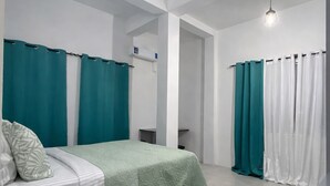 Une chambre à coucher avec un lit, des rideaux turquoise, une moquette verte et un mur blanc.