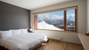 Une chambre avec une grande fenêtre, un lit, une table de chevet et une commode.
