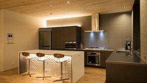 Une cuisine moderne dotée d’un îlot central, de tabourets de bar, d’appareils électroménagers intégrés et d’un plafond en bois.