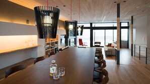 Un espace de salle à manger moderne, avec une longue table en bois, de nombreuses chaises et des lampes suspendues noires.