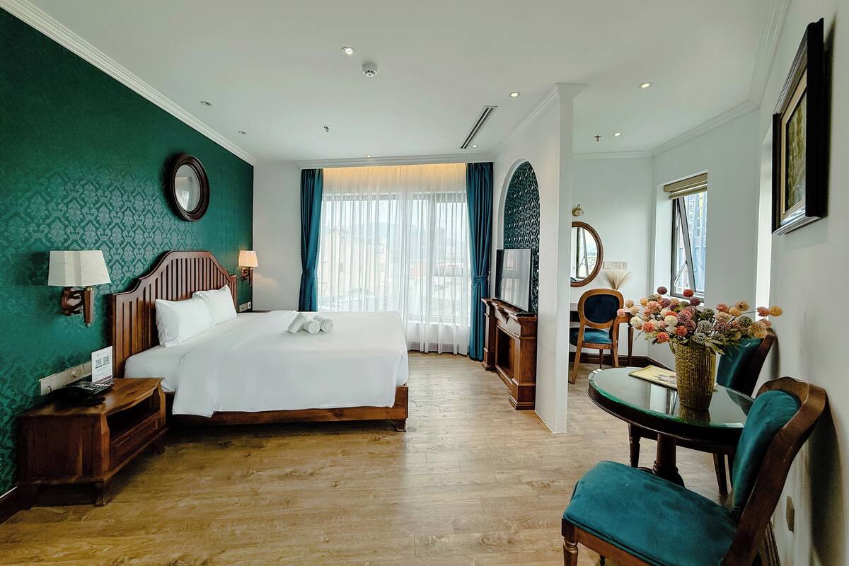 Una camera d'albergo con un letto, una scrivania, una sedia, una televisione e una finestra con tende.