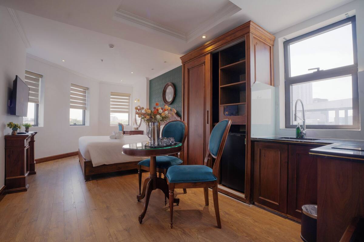 Una camera d'albergo con un letto, un tavolo da pranzo con sedie, un angolo cottura e un'ampia finestra.