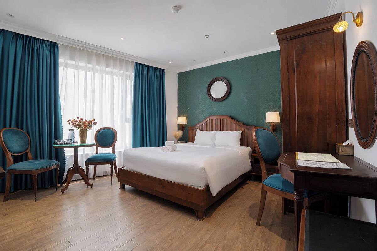 Camera d'albergo con un letto grande, due sedie, una scrivania, uno specchio e una finestra con tende.