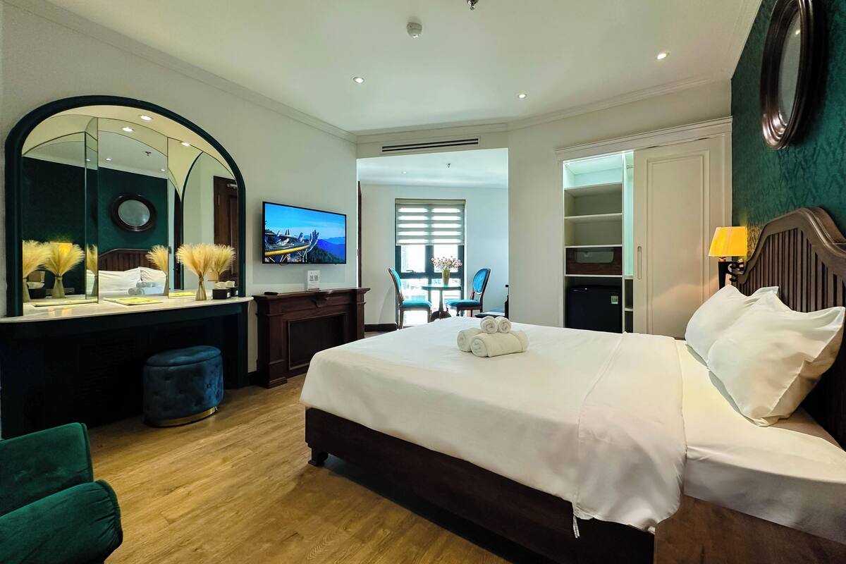 Una camera d'albergo con un letto grande, una televisione, una scrivania con una sedia, un armadio e uno specchio.