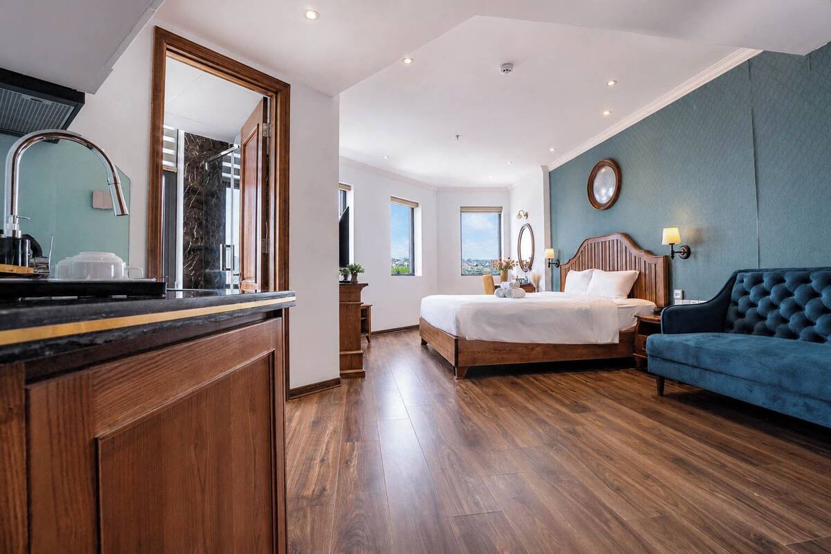 Una camera d'albergo con pavimento in legno, un letto, un divano blu, un bagno con uno specchio e vista sulla città.