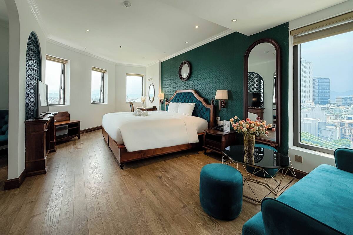 Una camera d'hotel con un letto grande, una scrivania, una sedia, uno specchio e vista sulla città.