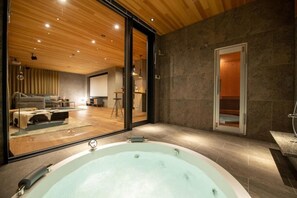 A modern bathroom with a large bathtub, a shower area, and a glass-enclosed living space with a sofa and a dining area. - Zaion (Kutchan)