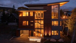 Ein modernes, mehrgeschossiges Haus mit großen Fenstern, einer sichtbaren Treppe und einer gut beleuchteten Außenfassade im Abenddämmerung.
