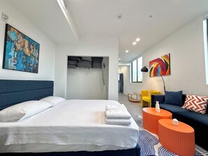 Une chambre d’hôtel moderne avec un grand lit, un canapé, une petite table et des œuvres d’art accrochées aux murs.