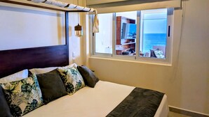 Un dormitorio con cama, ventana con vista al mar y lámpara colgante.