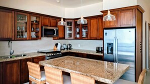 Una cocina moderna con armarios de madera, encimera de granito, electrodomésticos de acero inoxidable y sillas de mimbre.