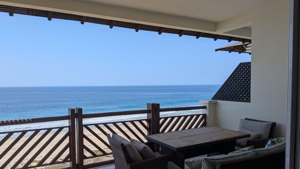 Un balcón con vista al océano, muebles de mimbre y barandilla de madera.