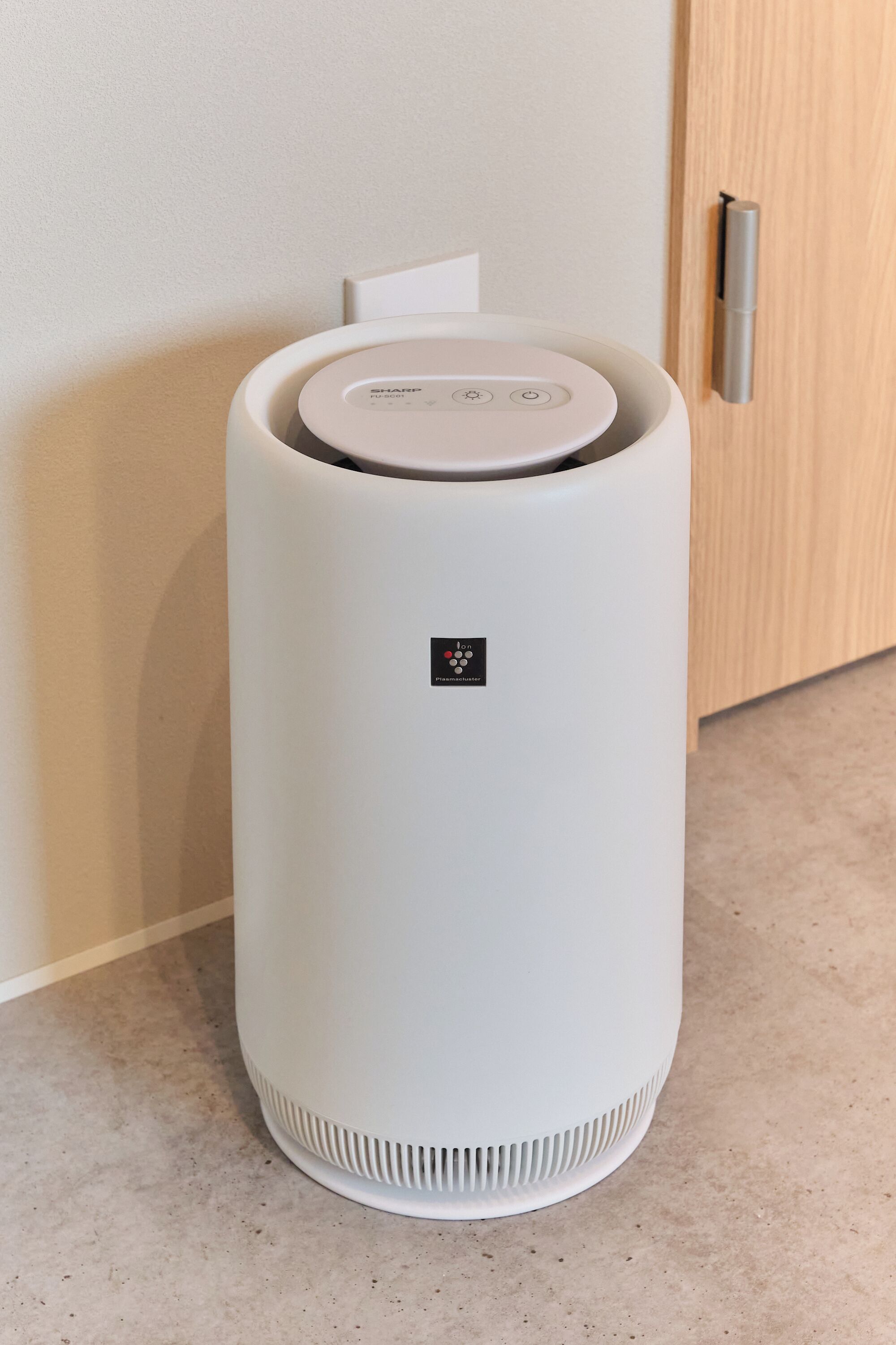 A white, cylindrical device with a control panel and a small logo, placed on a floor against a wall.
