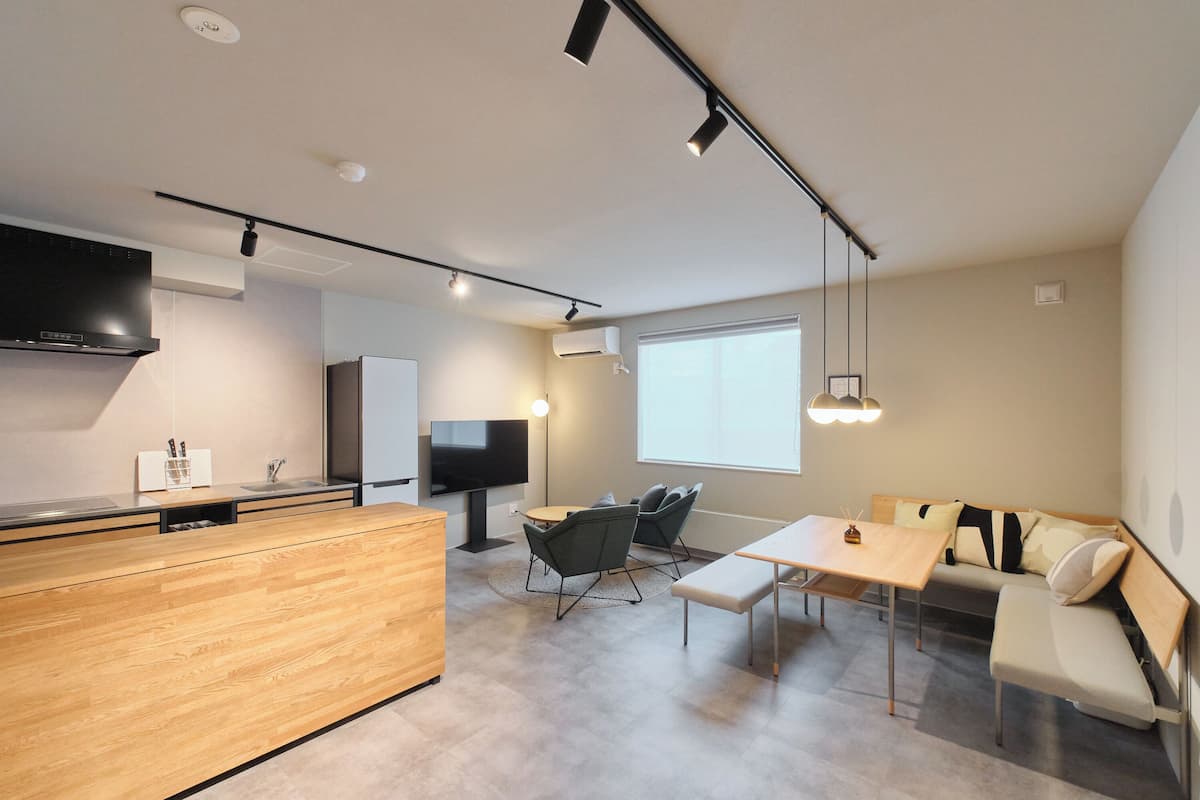 Una cocina moderna con encimera de madera, estufa integrada y televisor de pantalla plana. Hay un comedor con mesa y sillas, además de un sofá con reposabajos.