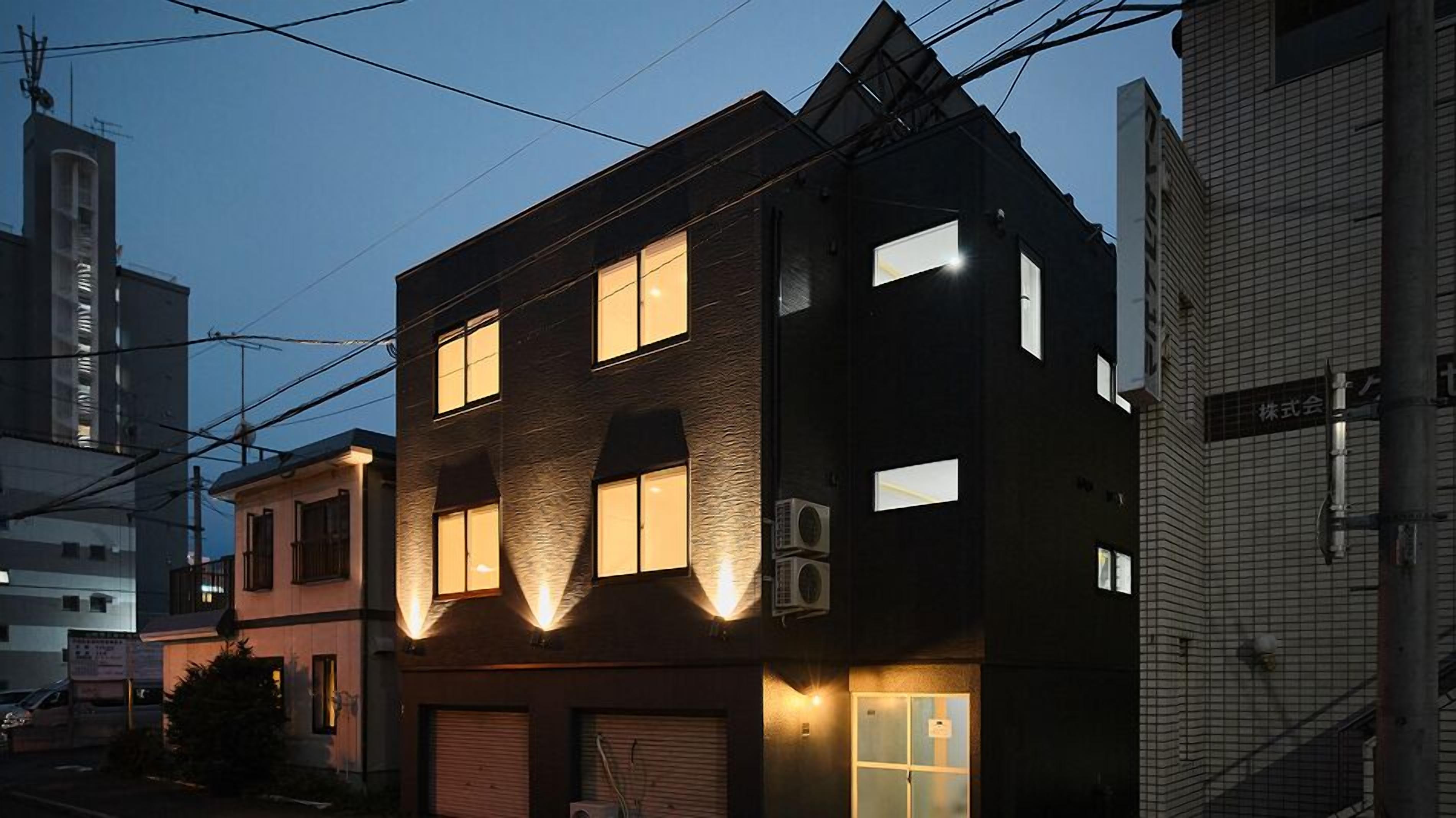 A multi-story building with a dark facade, multiple windows, and visible air conditioning units.