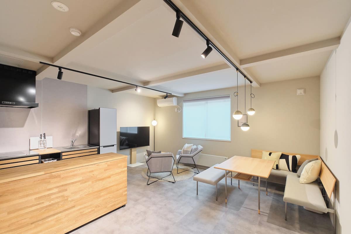 Cocina moderna con encimera de madera, estufa integrada y televisor de pantalla plana. Cuenta con un área de estar con mesa y sillas, y un amplio ventanal que proporciona luz natural.