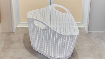 A white plastic laundry basket with a handle, placed on a beige floor.