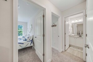 A bedroom with a bed, a bathroom with a sink and mirror, and a hallway. - Rae of Sunshine (Panama City Beach)