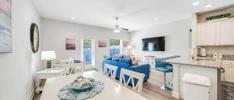 A modern kitchen with a TV, a dining area with a table and chairs, a blue sofa, and a ceiling fan.