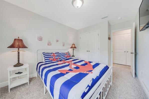 Une chambre à coucher avec un lit, deux lampes de chevet, une table de chevet blanche et une porte donnant sur une autre pièce.
