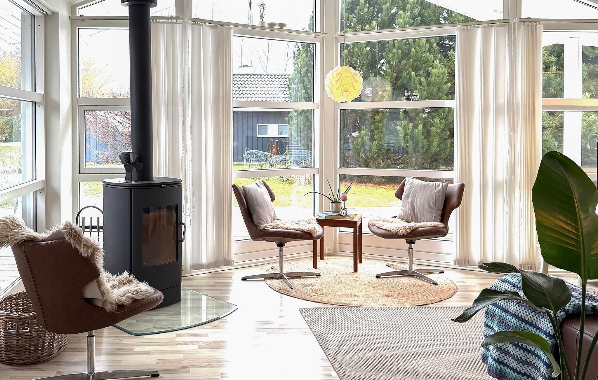 Una habitación acogedora con chimenea, dos sillones, una mesa y ventanas amplias.
