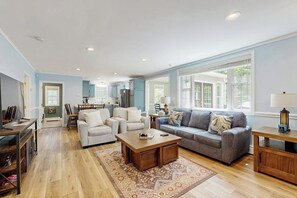 A spacious living room with a grey sofa, a wooden coffee table, and a patterned rug.