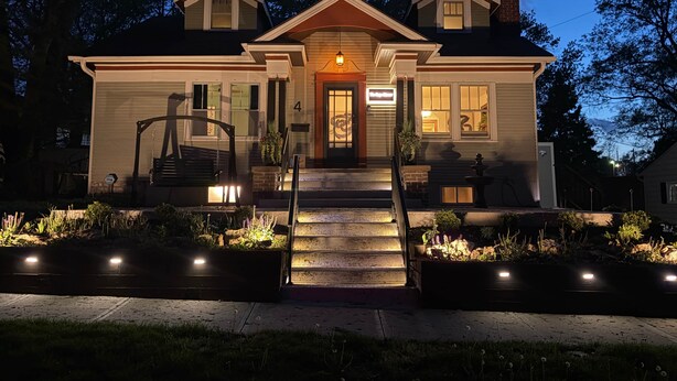 A two-story house with a front porch, a staircase, and a well-lit entrance. - Storybook Escape: Speakeasy + Hot Tub + Sauna + Cold Plunge - Walk to Downtown (Lee's Summit)