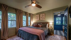 A bedroom with a bed, curtains, a ceiling fan, artwork, and a view through a window. - Storybook Escape: Speakeasy + Hot Tub + Sauna + Cold Plunge - Walk to Downtown (Lee's Summit)