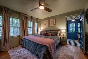 A bedroom with a bed, curtains, a ceiling fan, artwork, and a view through a window.