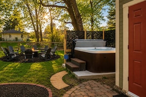 Un patio trasero con jacuzzi, mobiliario exterior y un camino de ladrillo.