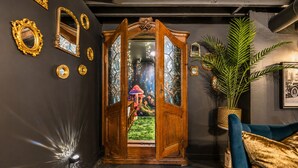 A room with a large wooden door, a blue sofa, and a potted plant. - Storybook Escape: Speakeasy + Hot Tub + Sauna + Cold Plunge - Walk to Downtown (Lee's Summit)