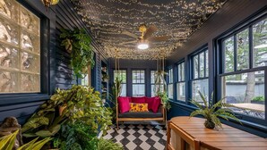 A room with a swing seat, large windows, ceiling lights, and various plants. - Storybook Escape: Speakeasy + Hot Tub + Sauna + Cold Plunge - Walk to Downtown (Lee's Summit)