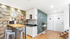 Eine moderne Küche mit Steinwand, einer Uhr, einer Mikrowelle und einem Spülbecken. Es gibt Hocker und einen kleinen Tisch.