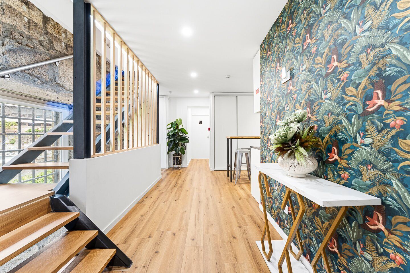 A modern interior with a wooden staircase, a plant, and a vibrant floral wall.