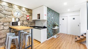 A modern kitchen with a stone wall, a clock, a microwave, and a sink. There are stools and a small table.