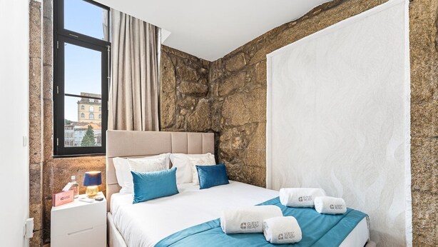 Ein Hotelzimmer mit Steinsturz, einem Bett mit blauer Bettwäsche, einem Nachttisch mit Lampe und einem Fenster mit Vorhängen.
