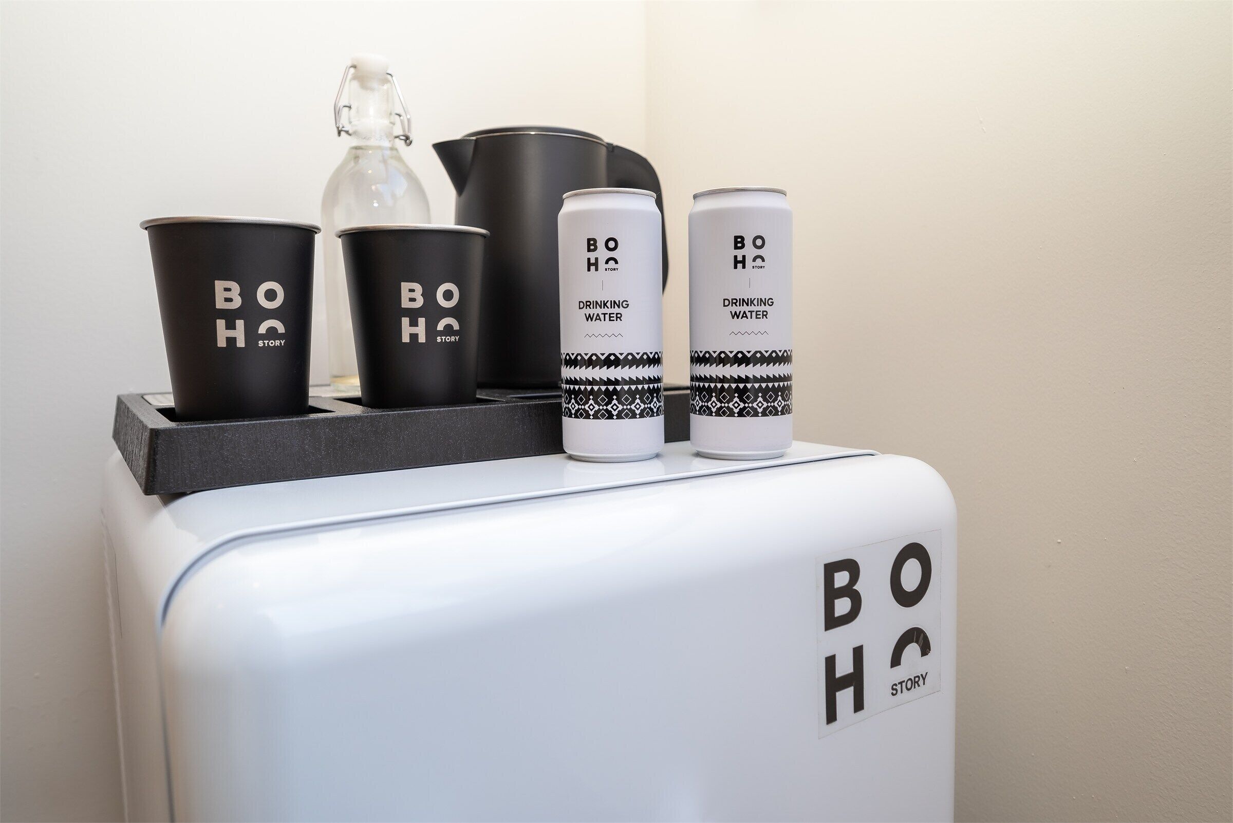 A refrigerator with the text 'BOHO STORY' on it, and two black cups with the same text, a white canister labeled 'DRINKING WATER,' and a black container.