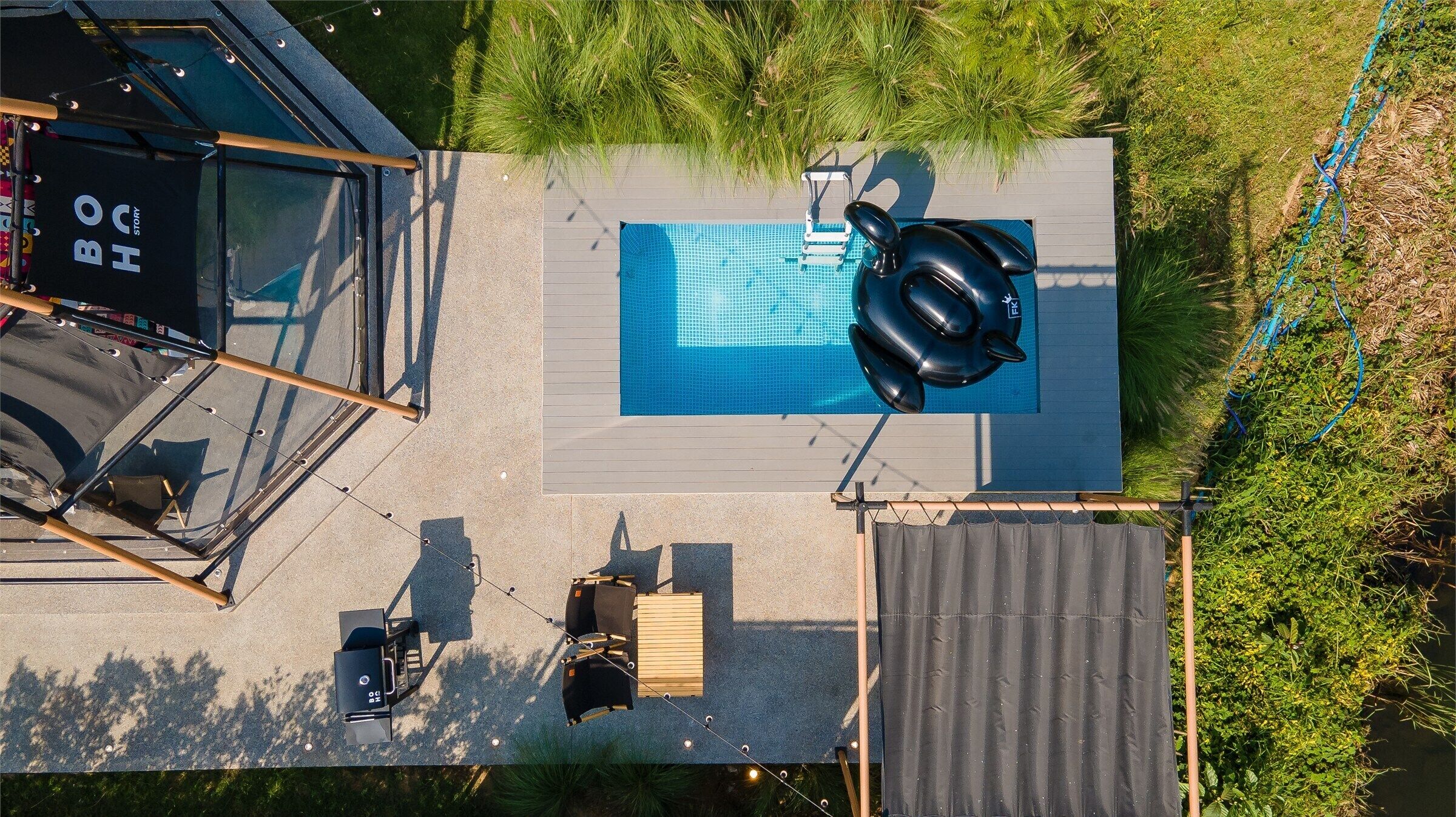 An aerial view of a rooftop pool area with a blue pool, inflatable rings, and a wooden deck.
