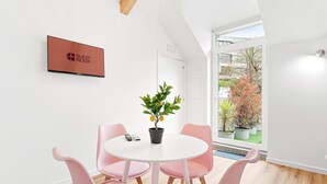 Een moderne kamer met een witte tafel, roze stoelen, een potplant en een wandtelevisie.
