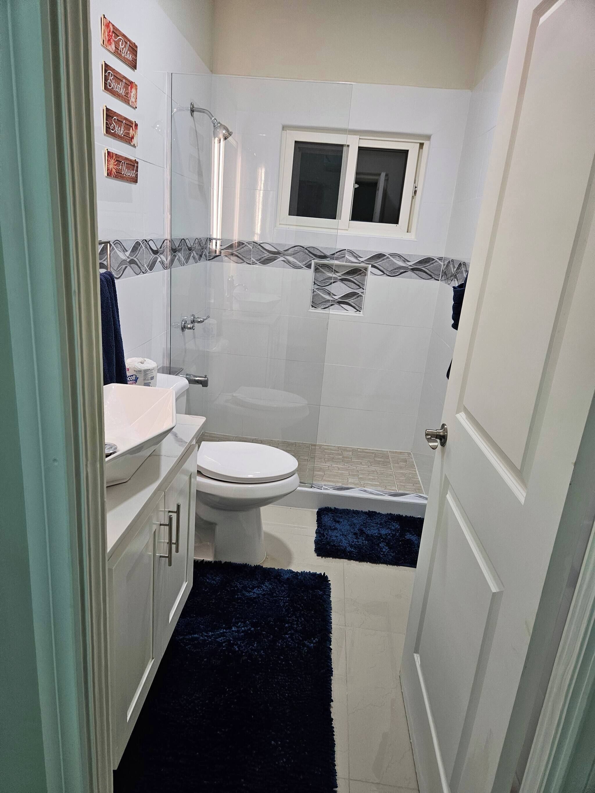 A bathroom with a toilet, sink, shower, and a small window.
