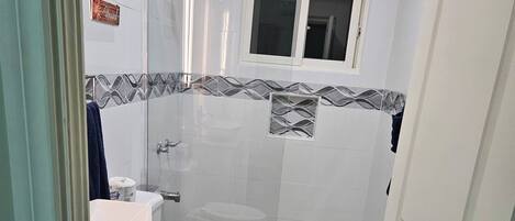 A bathroom with a toilet, sink, shower, and a small window.