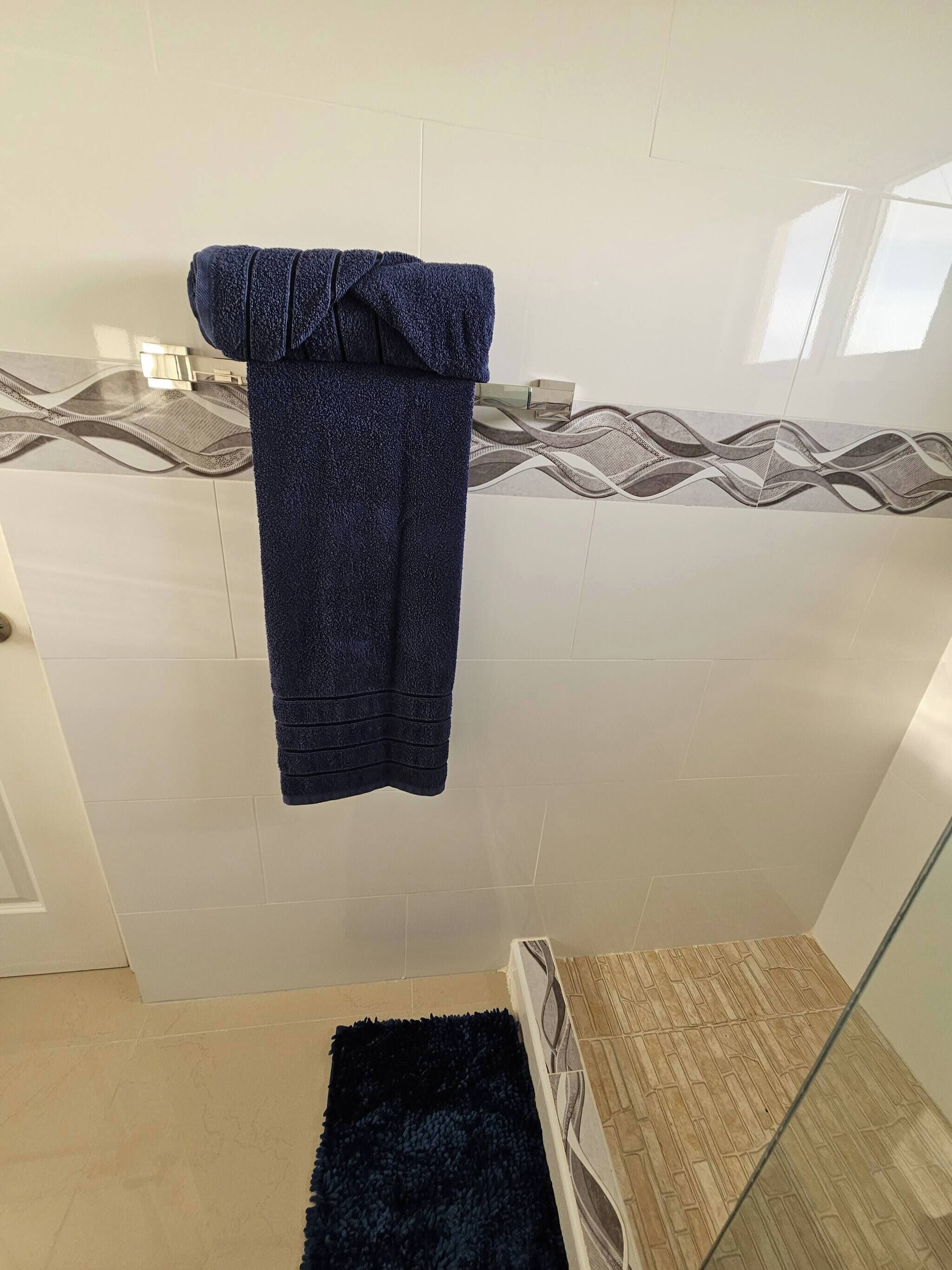 A bathroom with a towel hanging on a rack, a patterned tile backsplash, and a wooden floor.