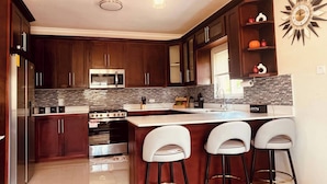 A modern kitchen with dark wood cabinets, stainless steel appliances, a large island with bar stools, and a decorative wall clock. - Tranquility Loft, Ocho Rios, Solar Powered (Ocho Rios)