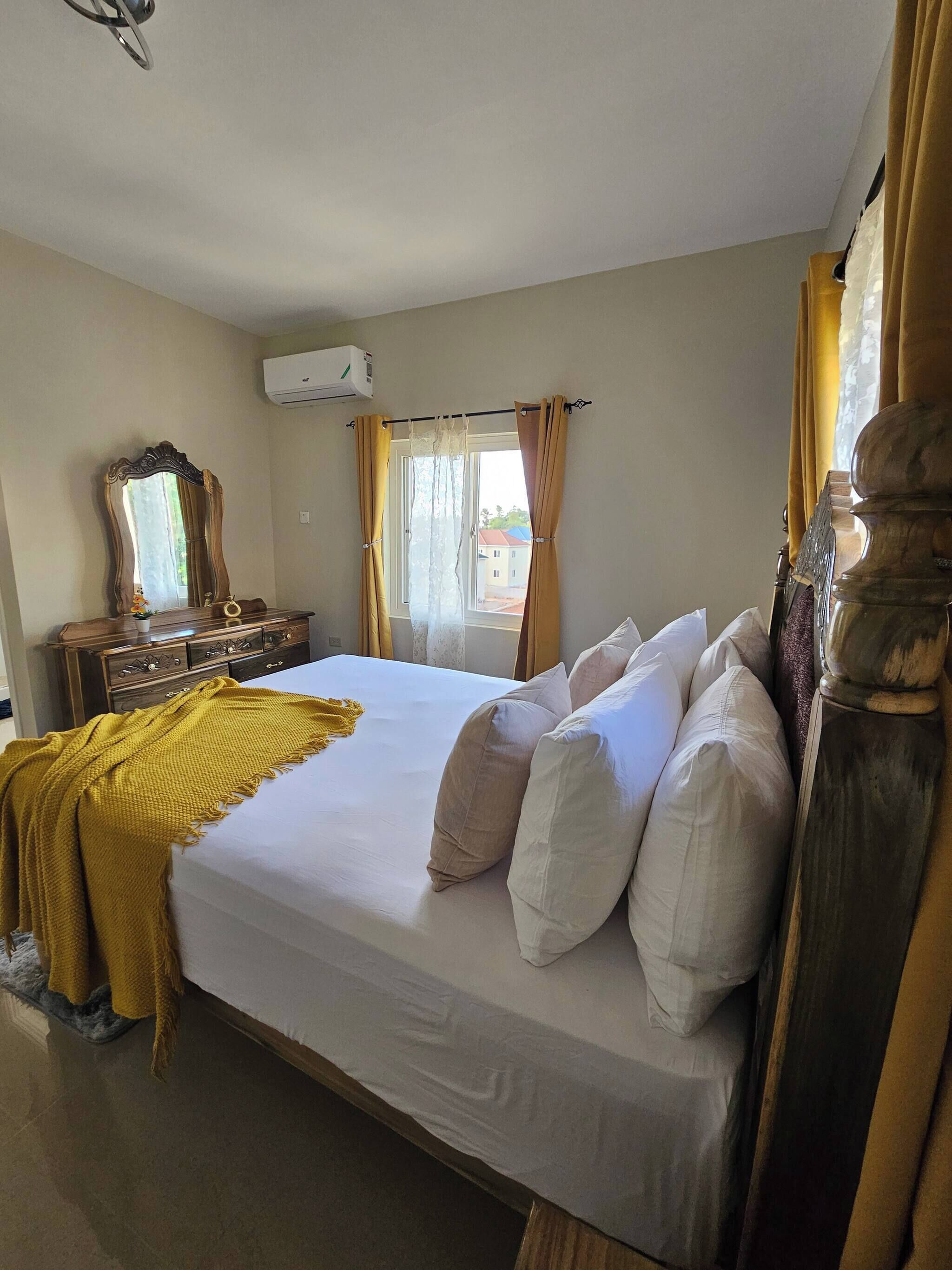 A bedroom with a bed, a dresser, a mirror, and a window with curtains.