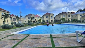 A swimming pool with tiled deck and grass borders, surrounded by residential buildings. - Tranquility Loft, Ocho Rios, Solar Powered (Ocho Rios)