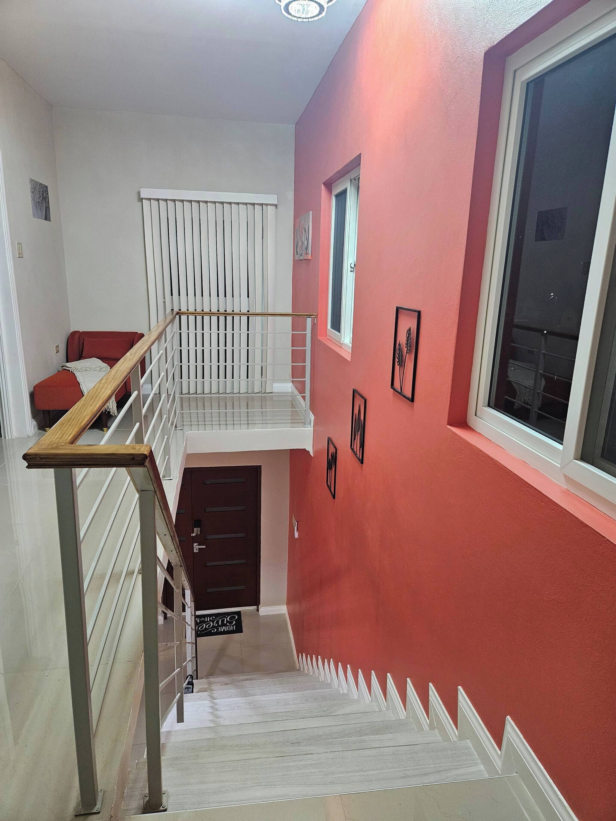 A staircase with a wooden handrail, a red wall, and a window with blinds.
