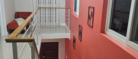 A staircase with a wooden handrail, a red wall, and a window with blinds.