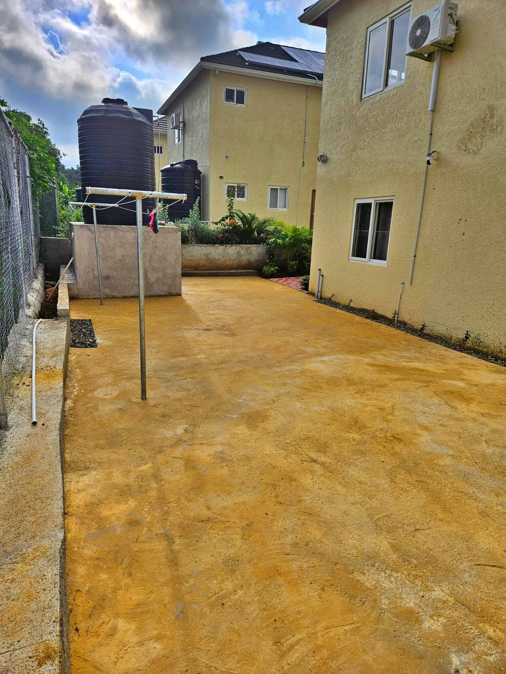A residential area with a concrete patio, a water tank, and a building with windows and a door.