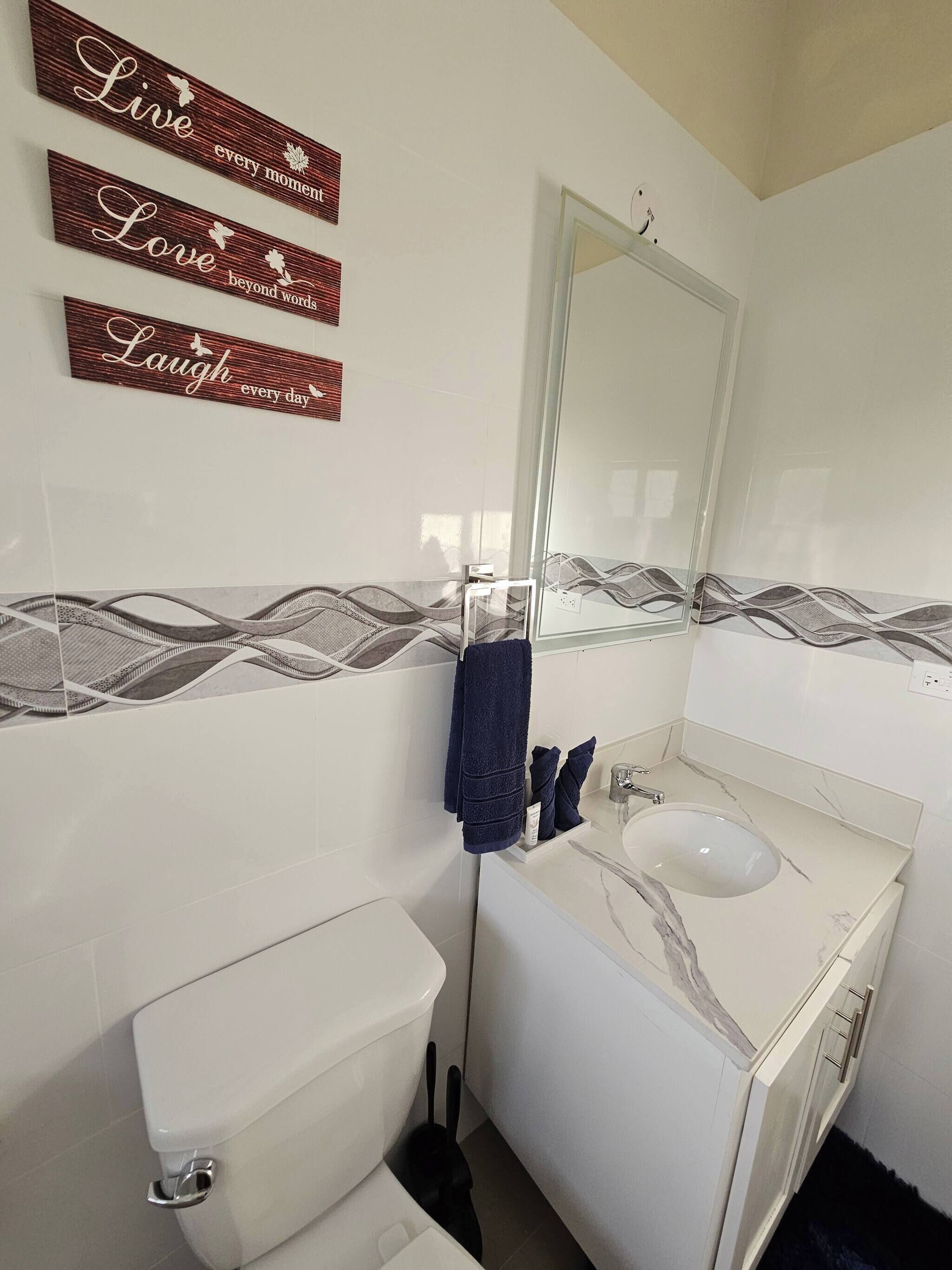 Un baño con inodoro, lavamanos y espejo. Hay letreros decorativos en la pared.